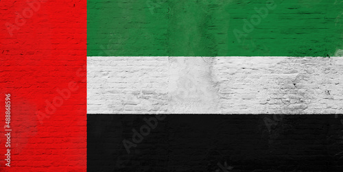 Full frame photo of a weathered flag of United Arab Emirates (UAE) painted on a plastered brick wall.