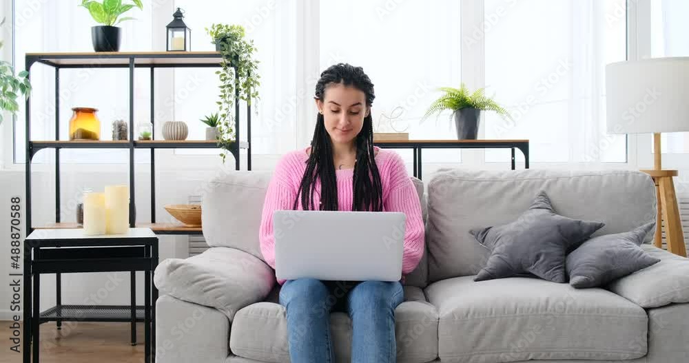 Happy young woman typing on laptop sitting on sofa at home Happy young woman typing on laptop sitting on sofa at home