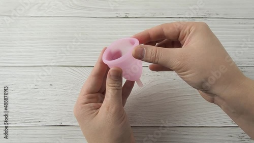 Woman hand holding menstrual cup and demonstrating labia folding methods. Intimate menstruation hygiene period. Zero waste alternative medical silicone products. Female health concept photo