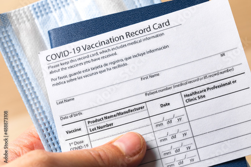 Passport with COVID-19 Vaccination record card and medical mask in hand. Close up view. - Image