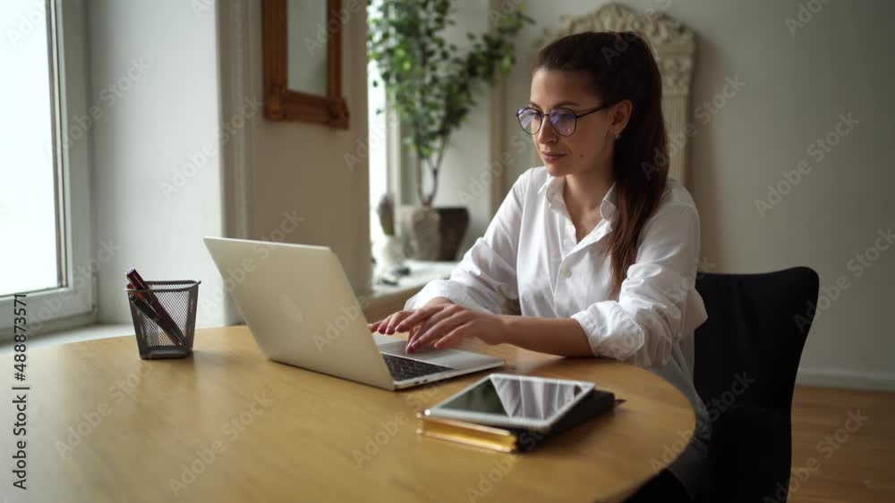 A young business woman working in an office uses a laptop, makes a monthly report on the project