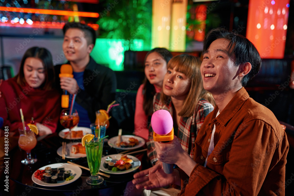 Asian friends singing into microphone at karaoke party at club Asian friends singing into microphone at karaoke party at club