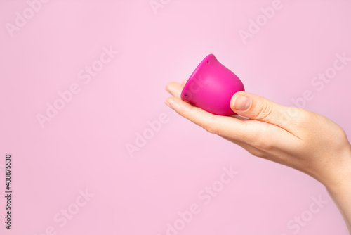 A young woman holds a pink menstrual cup in her hand. Pink colored background. Space for text. Eco-friendly silicone women's health cycle