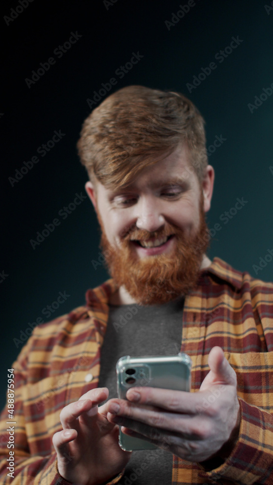 Redhead guy in modern plaid shirt look into the screen of new popular mobile phone Redhead guy in modern plaid shirt look into the screen of new popular mobile phone