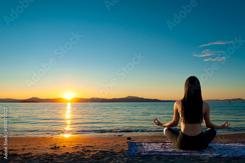 Jovem mulher sentada na beira do mar no fim de tarde meditando com um lindo por do sol. 