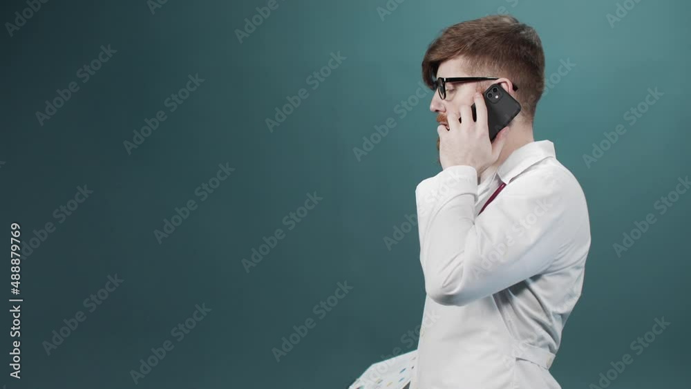 A man in a white gown talks on the phone and walks away with a tablet in his hand A man in a white gown talks on the phone and walks away with a tablet in his hand