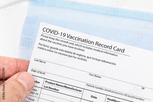 Womans hand holds coronavirus vaccination record card on background blue medical mask. Concept of defeating Covid-19 - Image