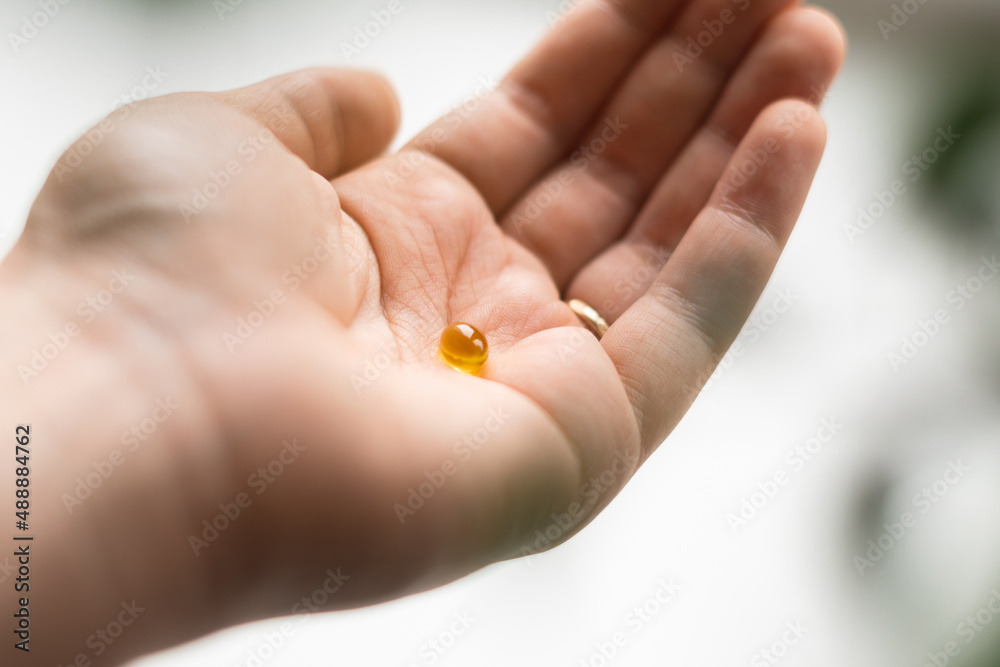 Close up of hand full of yellow softballs. Taking supplements, vitamin D or omega. Wellbeing biohacking concept