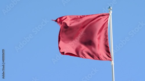 4K Slow Motion - Red flag blows violently in the wind against a clear blue sky