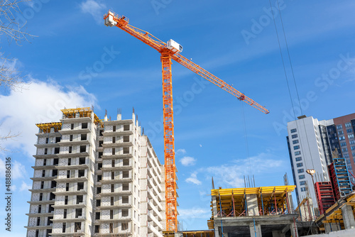 A bright tower crane on a construction site against the background of unfinished multi-storey buildings and blue sky photo