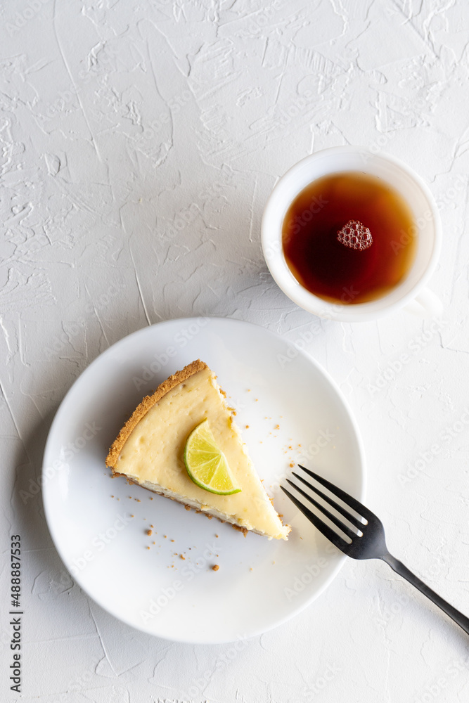 Slice of Lime Cheesecake on a White Plate with a Cup of Tea Slice of Lime Cheesecake on a White Plate with a Cup of Tea