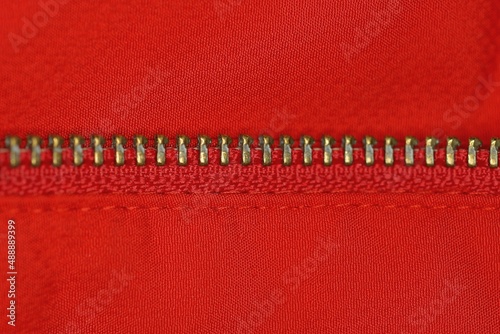 part of the yellow metal zip on the red fabric of the clothes © butus