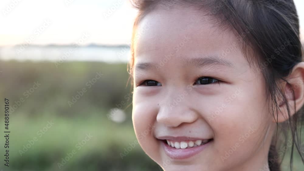 Portrait happy Asian little child girl smiling, laughing, looking at camera with beautiful sunset or sunrise in summer or spring nature outdoor background. Concept of portrait, happy children, family. Portrait happy Asian little child girl smiling, laughing, looking at camera with beautiful sunset or sunrise in summer or spring nature outdoor background. Concept of portrait, happy children, family.