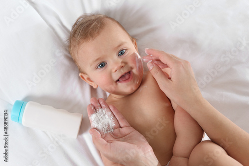 Mother applying dusting powder onto her baby on bed  top view