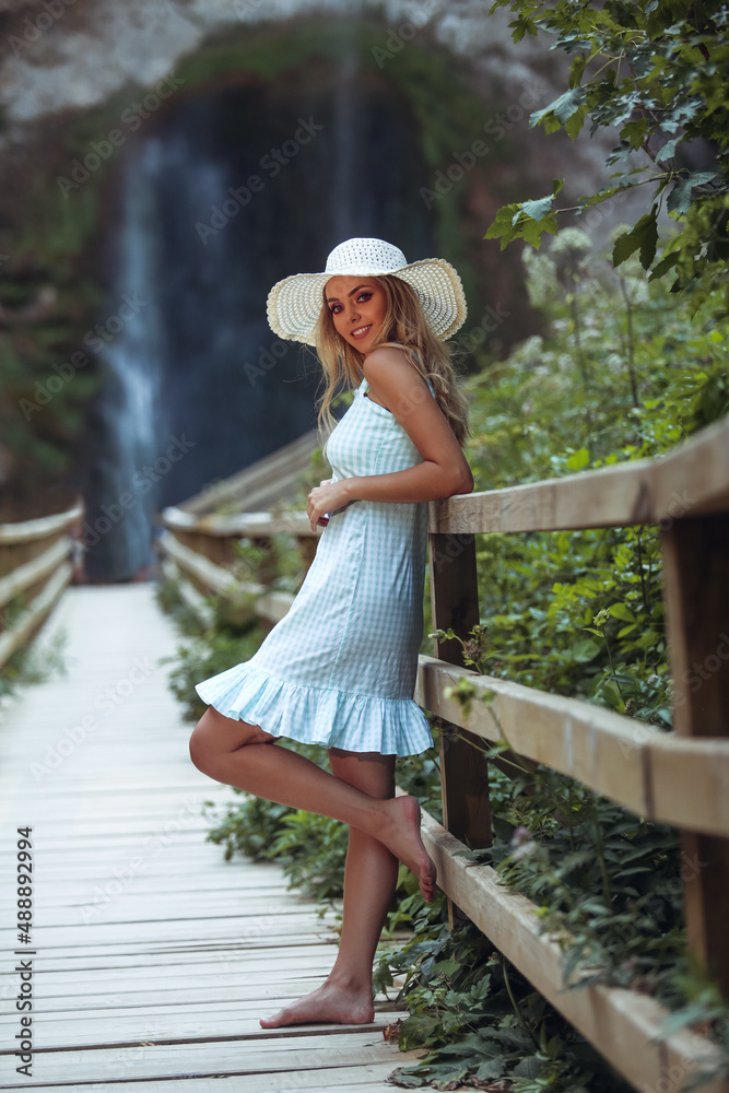 young woman in a dress and with a hat on her head by the waterfall
