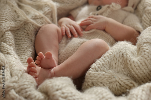 Adorable newborn baby lying on knitted plaid, closeup