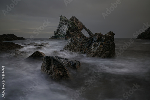Dramatic view with motion blur water of the Bow fiddle sea arch rock formation on the Moray coastline, Northwest highlands, Scotland. photo