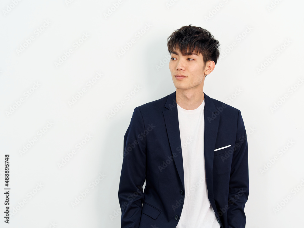 Portrait of handsome Chinese young man in dark blue leisure suit standing and posing against white wall background. Smiling and looking away, front view. Portrait of handsome Chinese young man in dark blue leisure suit standing and posing against white wall background. Smiling and looking away, front view.