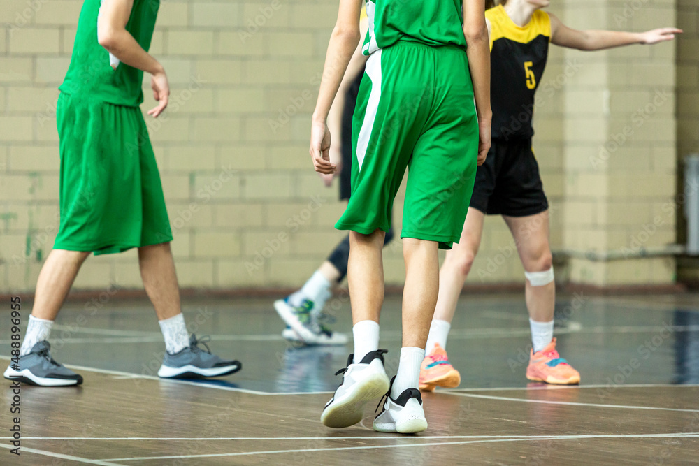 Basketball players in green team uniforms playing basketball. Boys dribbles a ball, teenagers practicing for a game in the school. Hobby, lifestyle