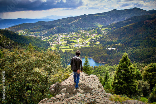 Photographie hombre parado en una roca frente a un abisco con  un paisaje y una ciudad en fre