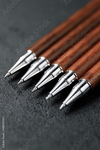 A set of expensive military pens made of rare wood, compositions on a dark background with attributes. Luxury gift pen.