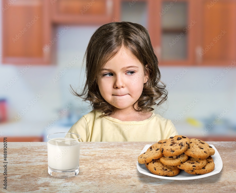 Portrait of sad girl holding glass of milk and dreaming, sitting on dinning table in kitchen interior Portrait of sad girl holding glass of milk and dreaming, sitting on dinning table in kitchen interior