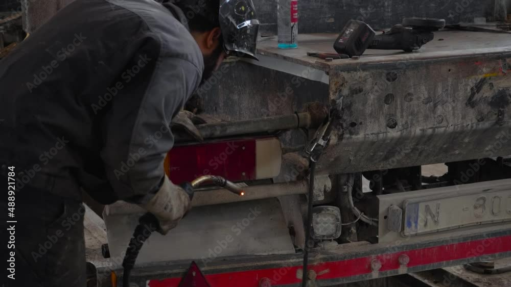 Worker inspects and welds dirty truck in workshop Worker inspects and welds dirty truck in workshop