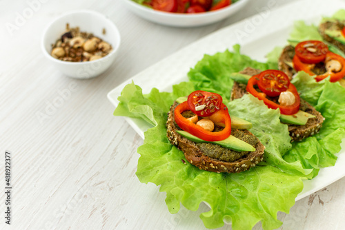 Vegan breakfast. Dietary nutrition. Sandwiches of grain bread with vegetables and nuts on a white plate on a white wooden table. Side view, close-up, space for text.