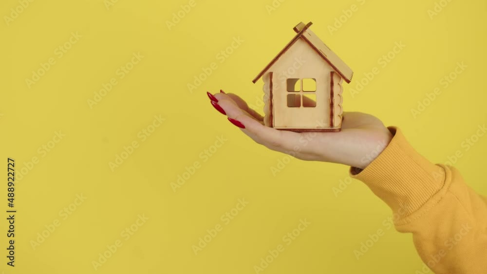 Young woman's hand with small wooden house. Crop unrecognizable person holding small toy house. Concept of purchasing new apartment and roof overhead.