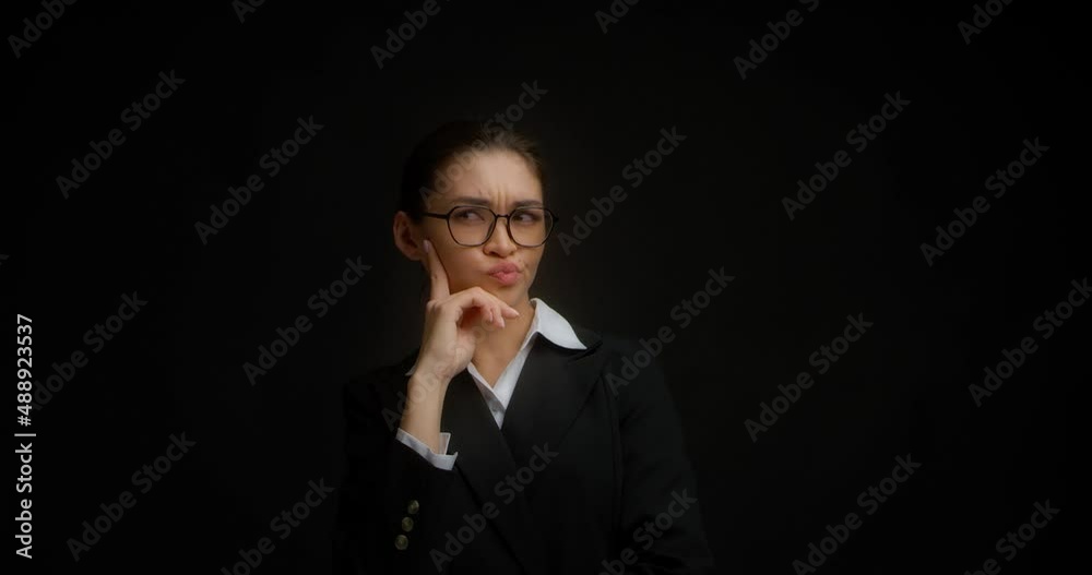 Thoughtful businesswoman, touches her chin, looks into the distance and dreams of the future, ponders ideas and strategies. Asian woman in glasses and a white shirt stands on a black background Thoughtful businesswoman, touches her chin, looks into the distance and dreams of the future, ponders ideas and strategies. Asian woman in glasses and a white shirt stands on a black background