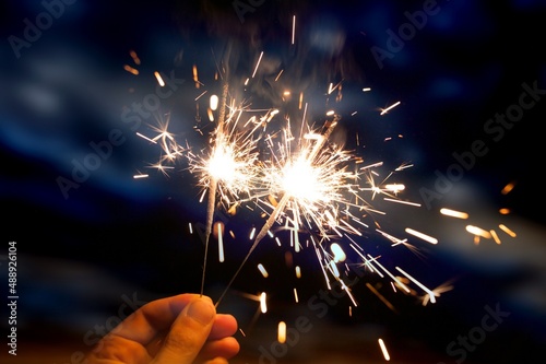 Hand holding sparkler firework firing with sky in background, concept of new year