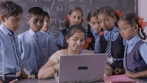 Young indian teacher teaching on laptop with school uniform students at classroom - concept of development, technology and digital education.