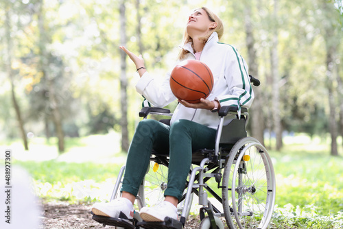 Young woman sitting in wheelchair holding basketball in park