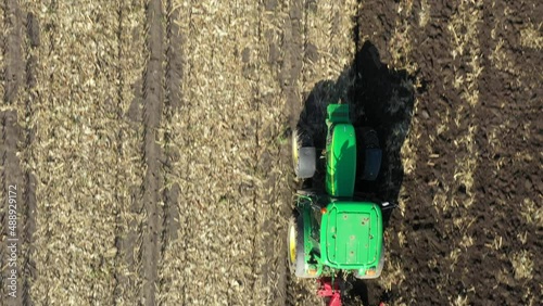 Aerial top view in dolly moving shot of tractor as plowing the ground on cultivated farm field, preparing soil for planting new crop next season.