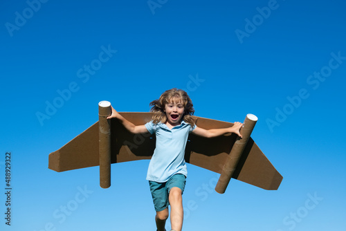 Kid with jet pack superhero. Child pilot against summer sky background. Boy with paper plane flight, toy airplane with cardboard wings, Imagination, kids freedom.
