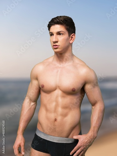 Sexy portrait of muscular handsome topless male model at the beach background.