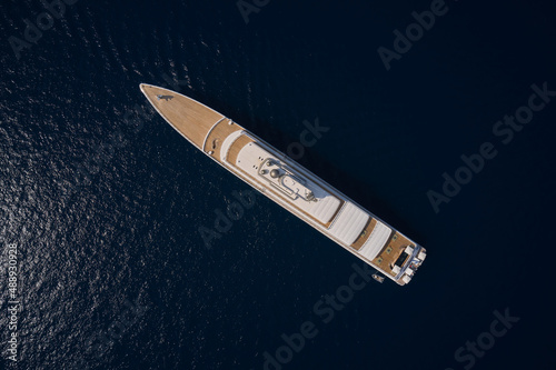 Big white super ship in the dark ocean aerial view. Big yacht for millionaires in the sea drone view. Luxurious white mega ship on dark water in the reflection of the sun top view