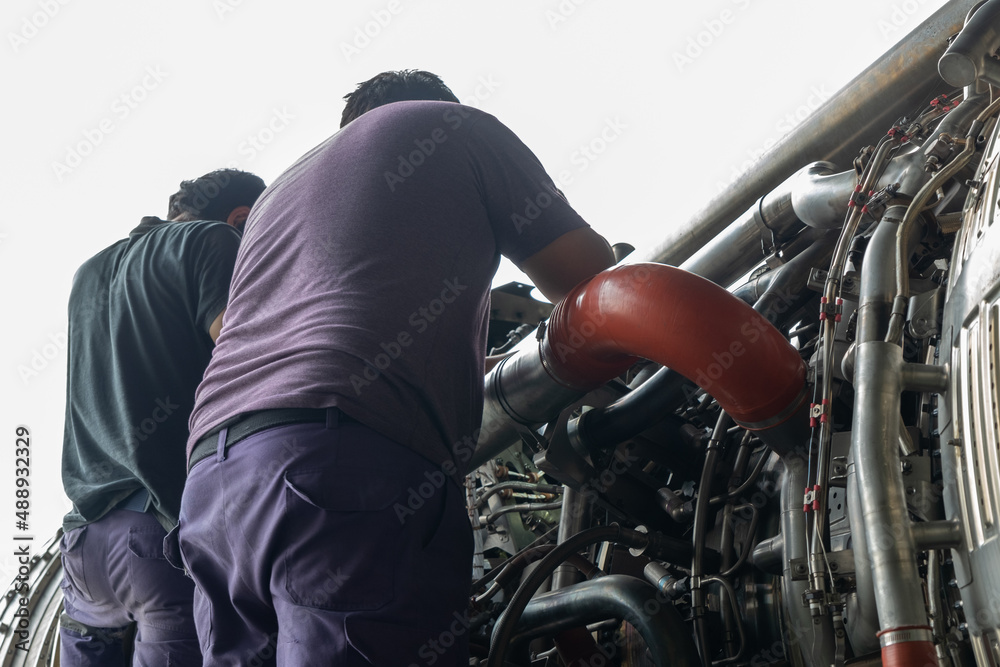 Obraz premium Technicians repair an aircraft gas turbine engine in the hangar. Close up of mechanics inspect an jet machine and system in aerospace industry.