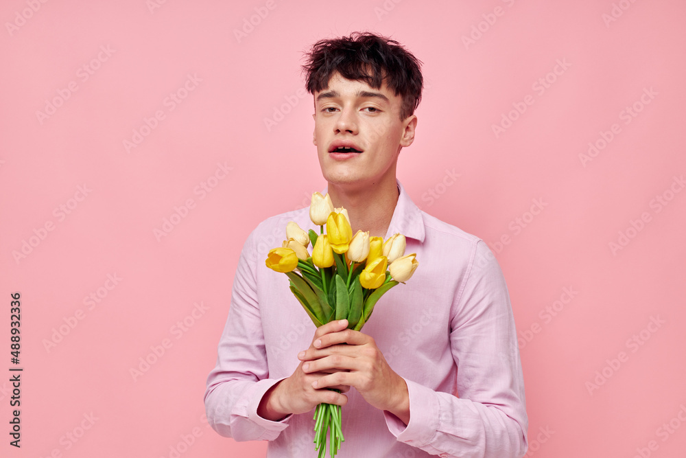 portrait of a young man in a pink shirt with a bouquet of flowers gesturing with his hands model studio portrait of a young man in a pink shirt with a bouquet of flowers gesturing with his hands model studio