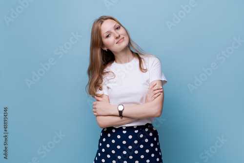 Photo cool attractive business woman with long hair friendly smiling responsible person, arms crossed with clock, wearing casual white t-shirt, isolated on blue color background