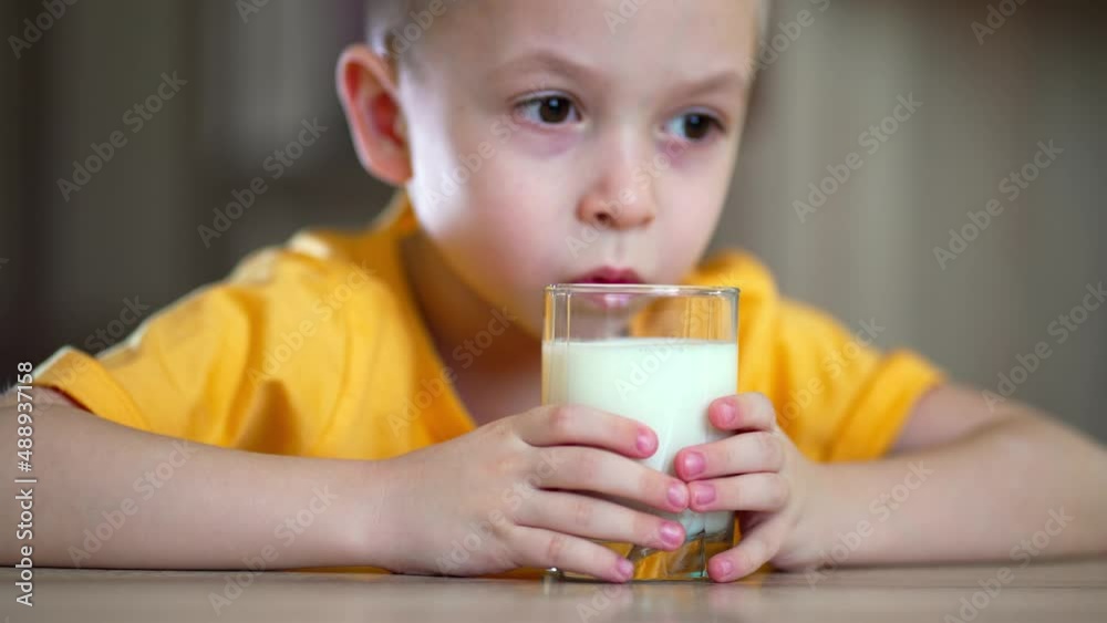 Boy holding a glass in her hands and drinks milk. Little boy drinks milk. Happy child has breakfast at home. Healthy child having breakfast. Boy holding a glass in her hands and drinks milk. Little boy drinks milk. Happy child has breakfast at home. Healthy child having breakfast.