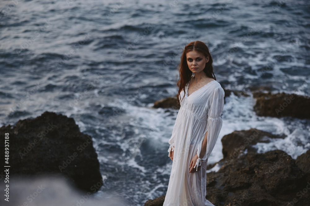 pretty woman with wet hair in wedding dress by the ocean rocks