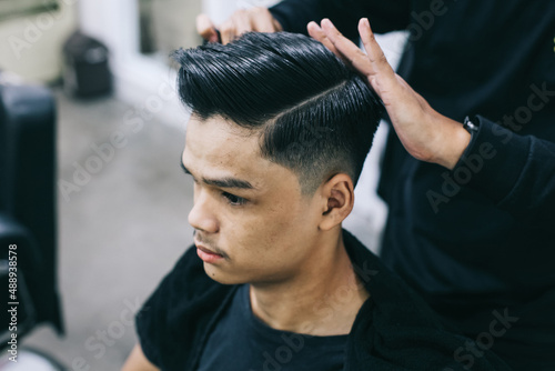 Young man at barbershop. Shave hair with the help of a hairdresser. Self-care, masculine beauty. Barber. Modern hair style