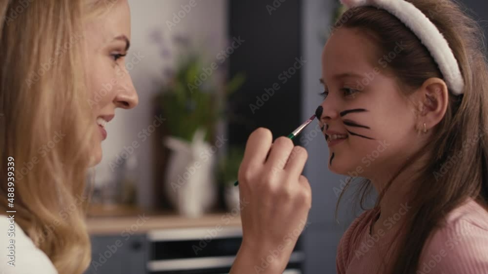 Side view of caucasian mother and daughter painting easter bunny on girl's face. Shot with RED helium camera in 8K Side view of caucasian mother and daughter painting easter bunny on girl's face. Shot with RED helium camera in 8K