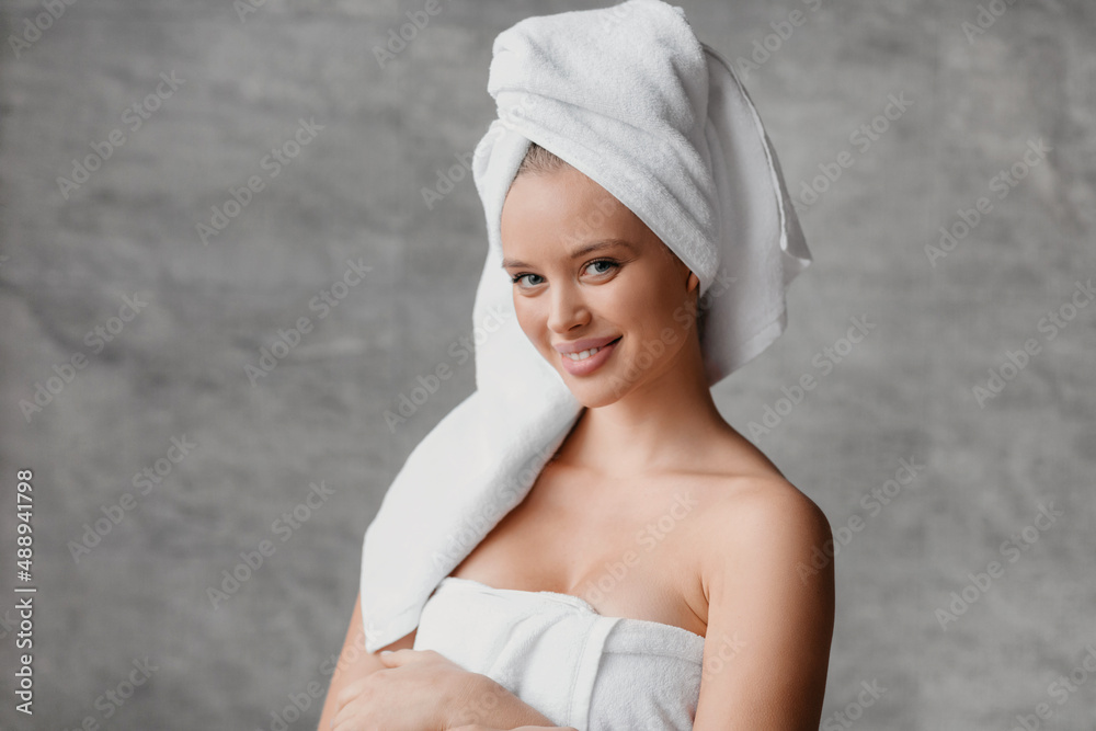 Obraz premium Spa and bodycare concept. Portrait pretty lady wearing bath towels and smiling at camera, standing in bathroom interior