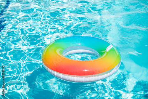 Blue aqua background. Pool float  rainbow ring floating in a refreshing blue swimming pool. Inflatable ring floating in pool on summer.