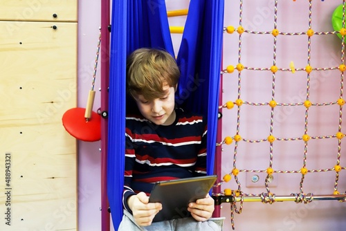 child boy watching cartoons on a tablet while sitting in a hammock at a children's center for the development of special children