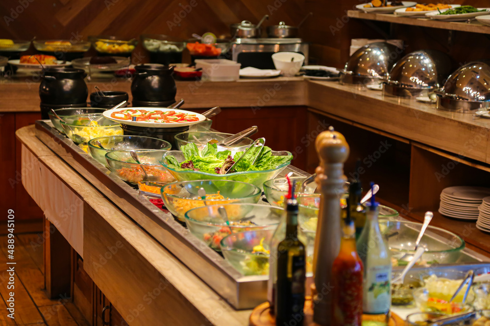 Fototapeta premium Lettuce and fruits in glass bowls on ice and caprese salad on white plate with stainless steel tongs hotel cold buffet chafing dish