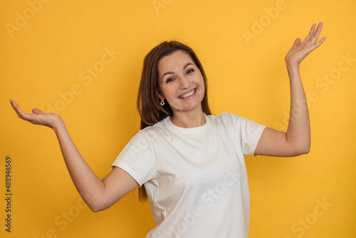 Portrait of a cheerful young woman on a yellow background with her hands raised up