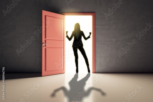 Successful businesswoman standing in front of bright door in concrete interior with shadow on floor. Future  success and dream concept.